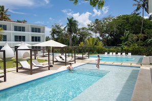A swimming pool with lounge chairs and umbrellas, surrounded by lush greenery and a modern building. - Breathtaking Cabarete Resort (Cabarete)