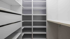 Ein schmaler, leerer begehbarer Kleiderschrank mit weißen Regalen und Schubladen.