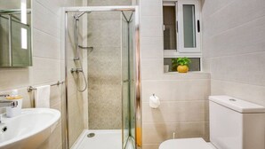 A bathroom with a glass-enclosed shower, a sink, a toilet, and a small window with a plant.