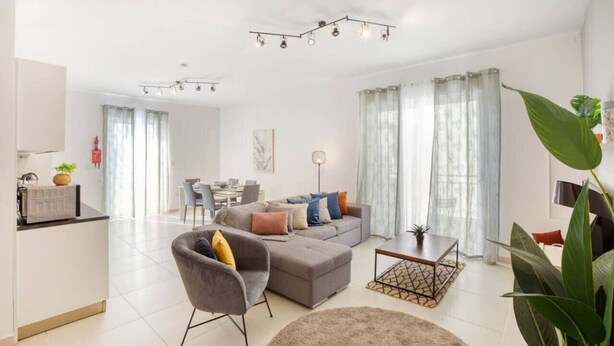A modern living room with a grey sofa, a coffee table, and a dining area in the background.