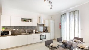 A modern kitchen with white cabinets, a built-in oven, and a dining area with a glass table set for four.