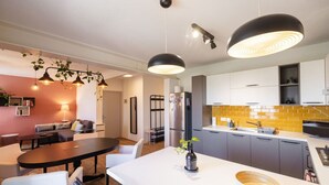 A modern kitchen with a central island, pendant lights, and a dining area with a table and chairs.