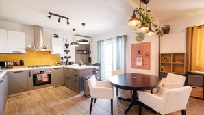 A modern kitchen with white cabinets, a central island, and pendant lighting. There is a dining area with a round table and white chairs.