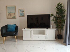 A living room with a flat-screen TV on a white cabinet, a black chair with a teal cushion, and a potted plant.