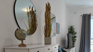 Una sala moderna con un armario blanco, un globo terráqueo y un espejo. Hay una planta sobre el armario y una silla con un cojín.
