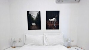 Habitación de hotel con cama, dos mesitas de noche, aire acondicionado y dos cuadros en la pared.