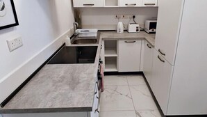 Una cocina moderna con armarios blancos, una campana extractora de acero inoxidable, una encimera y un suelo de baldosas.