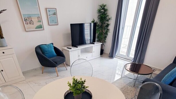 Una sala de estar moderna con una mesa redonda de vidrio, sillas transparentes, un sofá, un televisor y obras de arte en la pared.