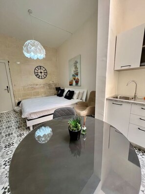Un dormitorio moderno con cama, una mesa redonda para comer con una planta, un reloj de pared y un cuadro.