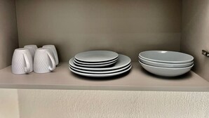 A shelf with white mugs, stacked plates, and a bowl. - Cottonera Cara: Cozy Room with Terrace in the Heart of Bormla (Bormla)