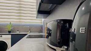 A modern kitchen with a marble countertop, a washing machine, and a compact refrigerator.