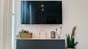 A modern living room with a flat-screen TV mounted on the wall, a dark grey cabinet with decorative items, and a potted plant.
