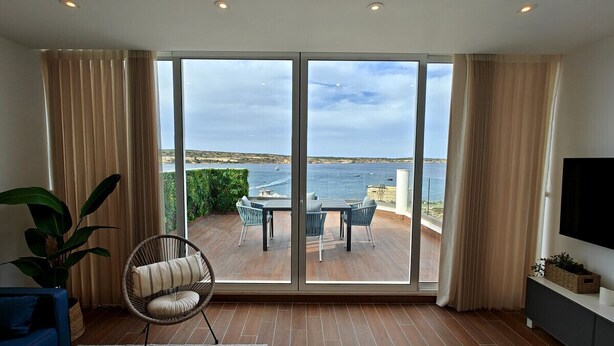 A spacious living room with a large sliding glass door leading to an outdoor patio with a view of the sea.