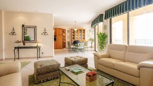 Ein Wohnzimmer mit Sofa, Hocker und Couchtisch. Im Hintergrund ist eine Essecke mit Tisch und Stühlen zu sehen.