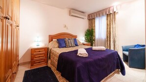 Ein Schlafzimmer mit einem Bett, einem Nachttisch, einer Lampe, einem Sessel und einer Klimaanlage.