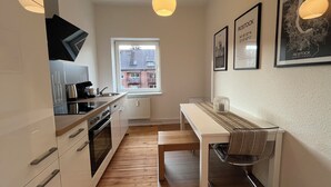 A compact kitchen with modern appliances, a window with a view of buildings, and a small dining area with a bench and chair. - Coastal berth I (Rostock)