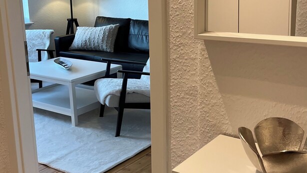 A modern living room with a sofa, a coffee table, and a painting of a beach scene. - Coastal berth I (Rostock)