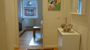 A narrow hallway with a wooden floor leading to a kitchen area with white cabinets and a window. - Coastal berth I (Rostock)