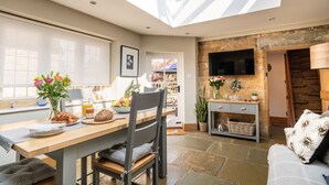 A modern kitchen with a skylight, a dining area with a wooden table and chairs, and a cozy living space with a sofa and a TV mounted on a stone wall. - A beautiful quintessential Cotswold Cottage - Honeysuckle Cottage, Stanton (Stanton)