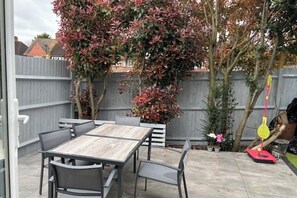 A patio with a wooden table and chairs, surrounded by a wooden fence and various potted plants.