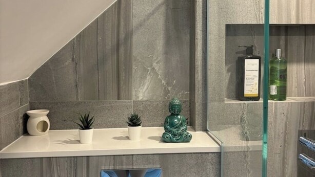 Casa de banho com bancada branca, uma estátua verde de Buda, uma pequena planta em vaso, um vaso branco e uma embalagem de sabonete líquido.