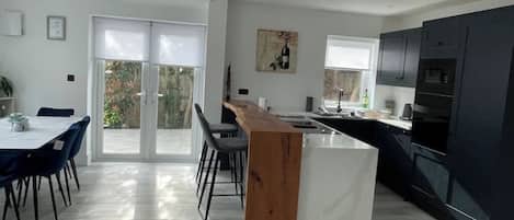Una cocina moderna con armarios oscuros, una isla de madera y una zona de comedor con mesa y sillas.