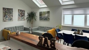 Uma sala de estar moderna com uma mesa de centro de madeira, dois sofás cinzas, uma janela grande e claraboias.