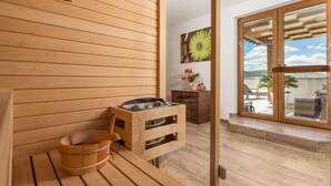 Un sauna en bois, avec un banc et des seaux, un meuble en bois et une vue sur l’extérieur grâce à une porte en verre.