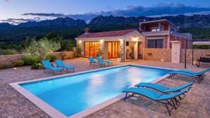 Une maison moderne avec une piscine, entourée de montagnes.