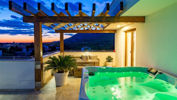 Une terrasse sur le toit avec un jacuzzi, des plantes en pot et une vue sur le paysage urbain au coucher du soleil.