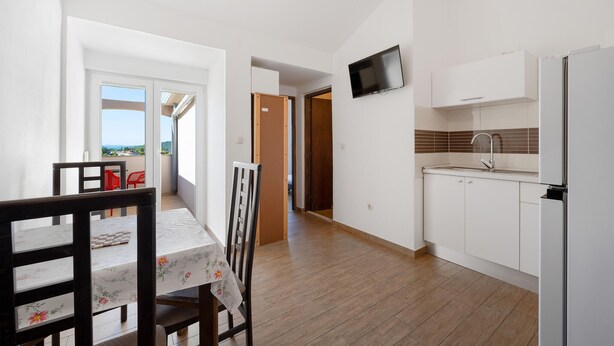 A modern kitchen with white cabinets, a built-in TV, and a dining area with a table and chairs. - Amazing apartment in Pirovac with lake view (Pirovac)
