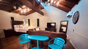 Ein gemütliches Zimmer mit einem Bett, einem Fernseher, einem Esstisch mit Stühlen und Holzboden.