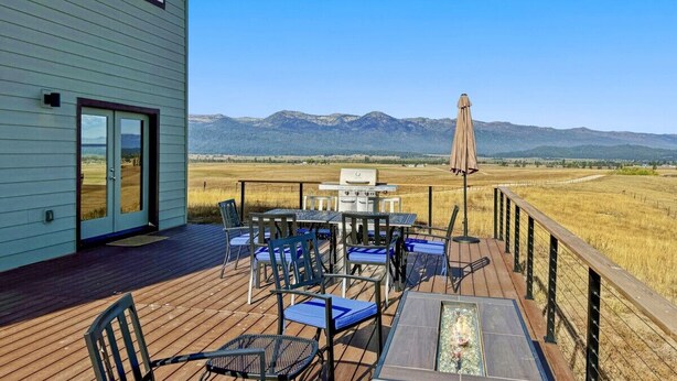 Une terrasse avec coin salon extérieur, un barbecue et une vue sur les montagnes.