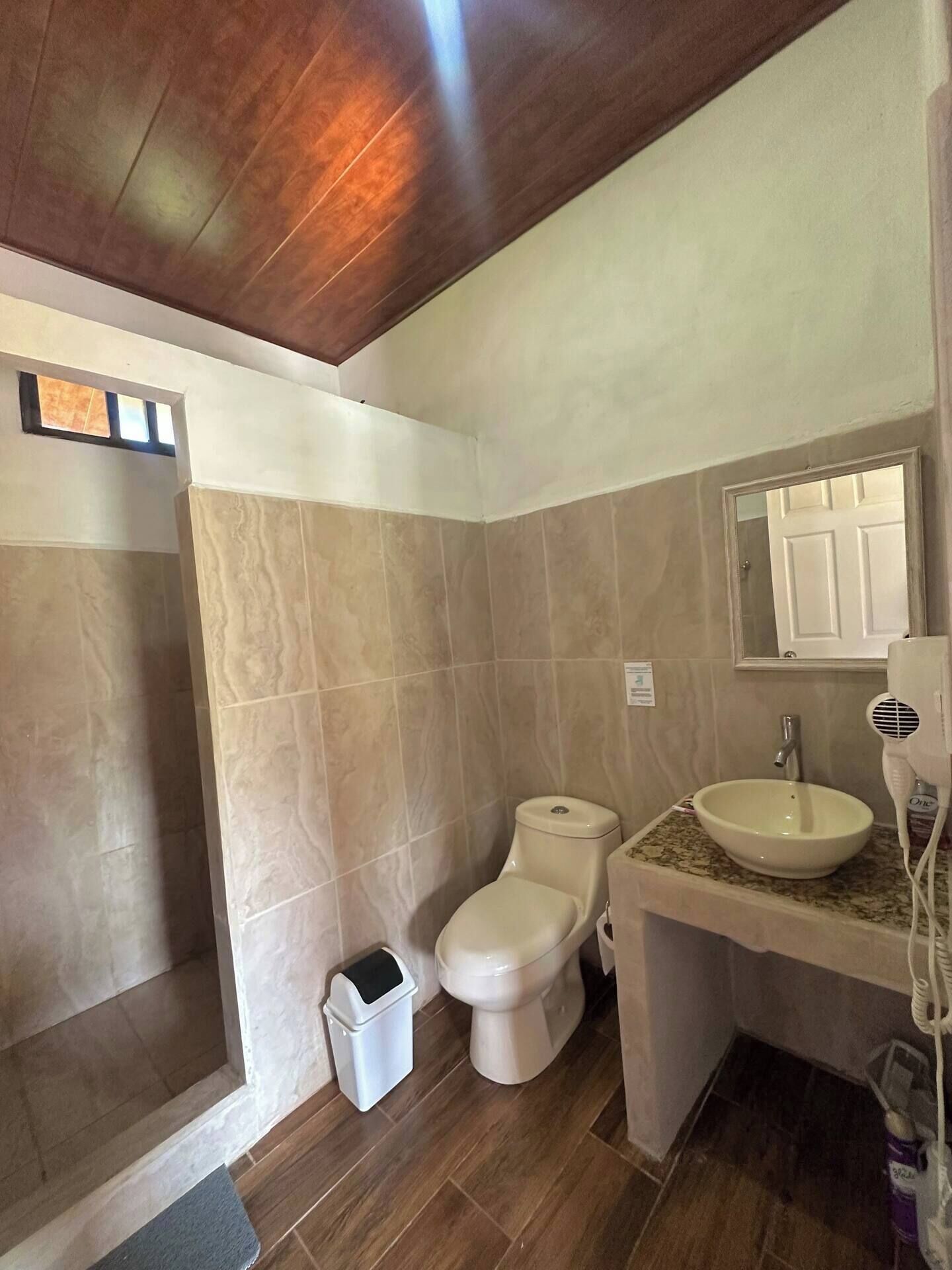 Casa de banho com chuveiro, sanita, lavatório e secador de cabelo.