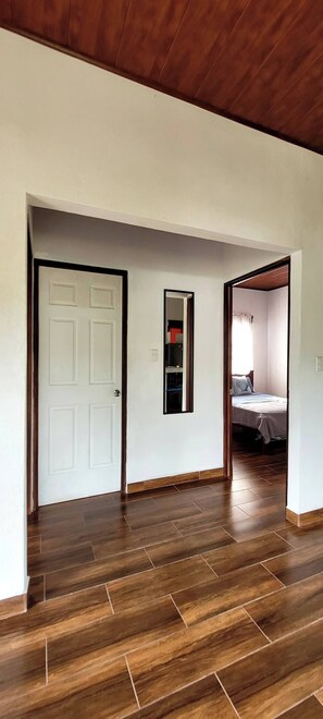 Un pasillo con piso de madera, una puerta blanca y un espejo en la pared.