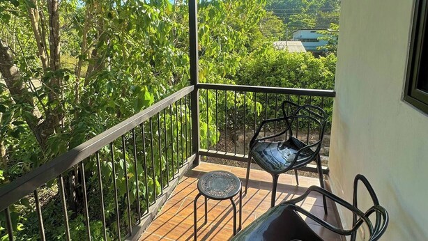 A balcony with a view of a lush green landscape, a wooden ceiling, and two metal chairs. - Villa Marina (Nosara)