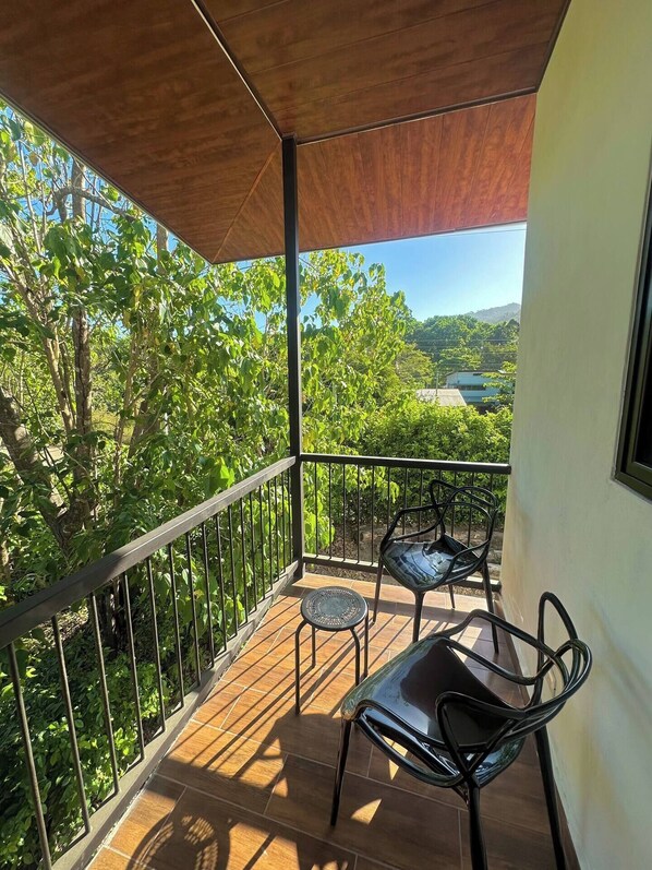 Un balcón con vistas a un paisaje verde exuberante, techo de madera y dos sillas de metal.