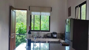 A kitchen with a large window, a refrigerator, a sink, and a countertop. - Villa Marina (Nosara)