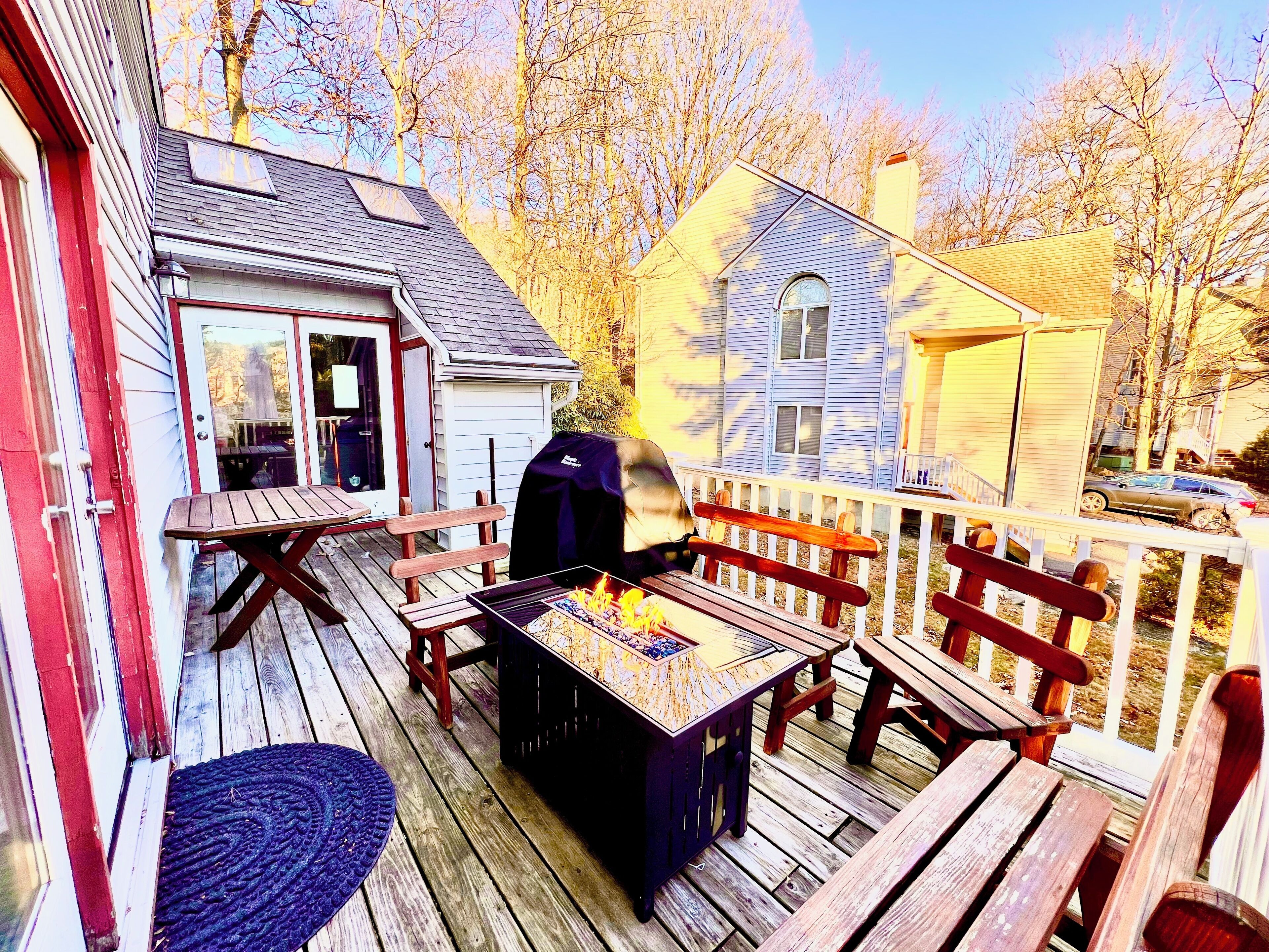 A wooden deck with a barbecue grill, picnic table, and benches.