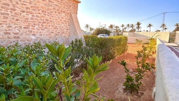A stone building with a paved pathway leading to a white car parked in the distance. - Golden Sand House 2 (Hammamet)