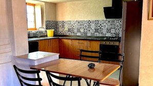 A compact kitchen with a wooden table and chairs, a tiled backsplash, and a refrigerator. - Golden Sand House 2 (Hammamet)