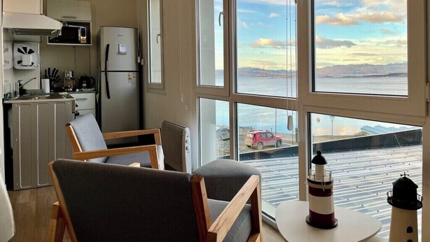 A modern kitchen with a view of the sea, a dining area with chairs, and a table with a bottle. - Studio with great view of the Beagle Channel (Ushuaia)