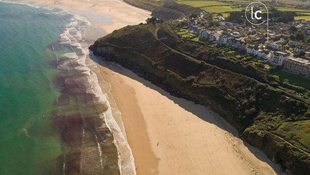 An aerial view of a coastal area with a sandy beach, a small town with houses, and a clear sky. - Offshore -  Carbis Bay (Carbis Bay)