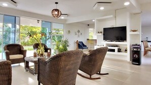 Un salon moderne avec des meubles en osier, un téléviseur à écran plat et une grande fenêtre donnant sur un paysage verdoyant.