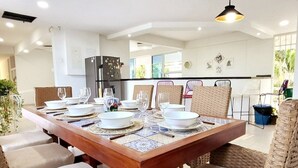 Un coin repas avec une longue table en bois, dressée pour six personnes, entourée de chaises en osier.