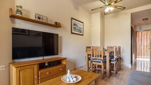 Ein Wohnzimmer mit Flachbildfernseher, Holzmöbeln, Deckenventilator und einem Essbereich mit Stühlen und Tisch.