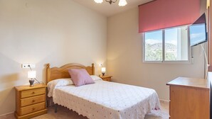 Ein Schlafzimmer mit Bett, Nachttischen, einem Schminktisch und einem Blick aus dem Fenster. Eine Deckenleuchte vervollständigt den Raum.