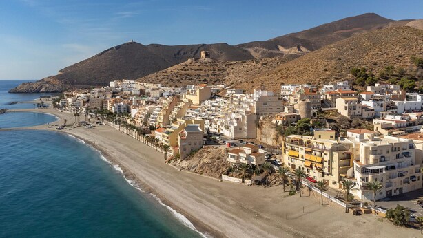 Eine Küstenstadt mit Gebäuden direkt am Strand und einem Berg im Hintergrund.