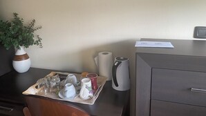 Habitación de hotel con un escritorio, un florero con hojas verdes, una bandeja con tazas, platillos, una tetera y un documento en el escritorio.