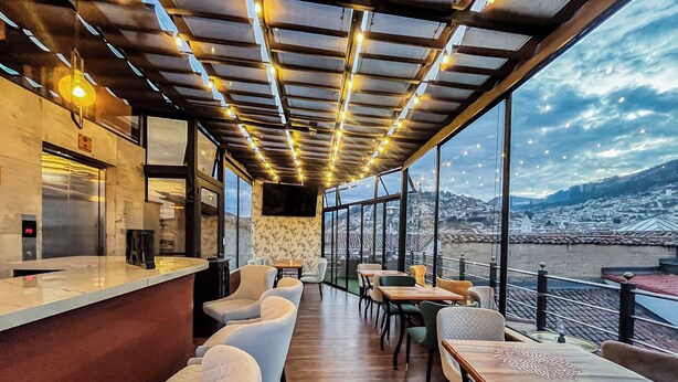 A restaurant with a bar area, seating, and large windows offering a view of a city and hills. - Hotel & Rooftop King Experience by David (Quito)